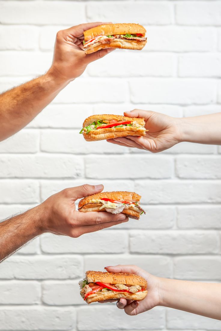 four hands holding sandwiches in front of a brick wall