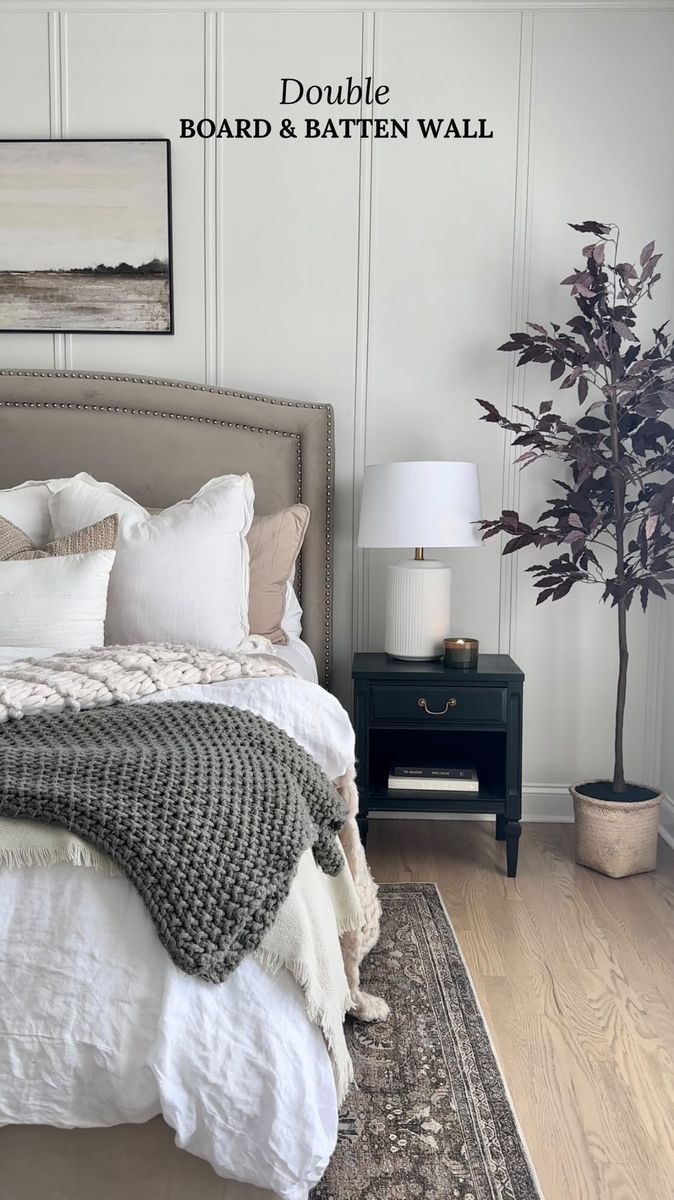 there is a bed with white sheets and blankets on top of it, next to a potted plant