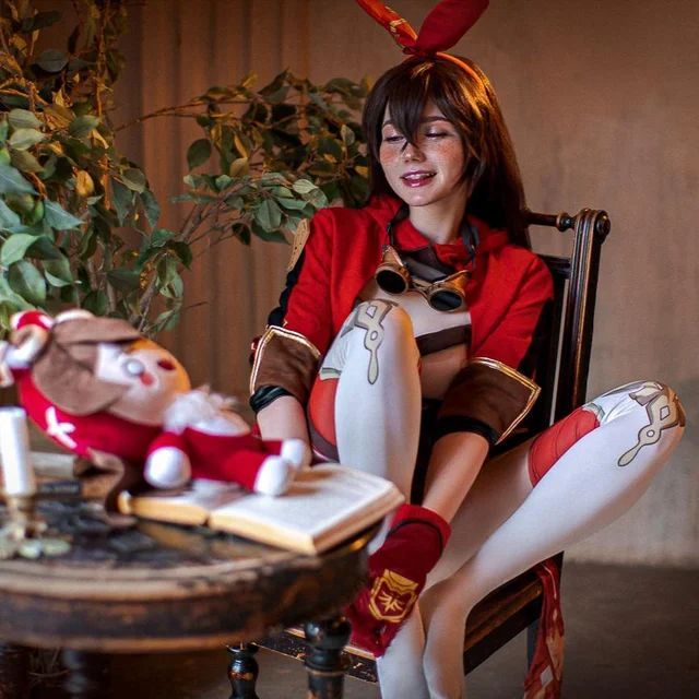 a woman sitting in a chair next to a christmas tree and stuffed animal on top of a table