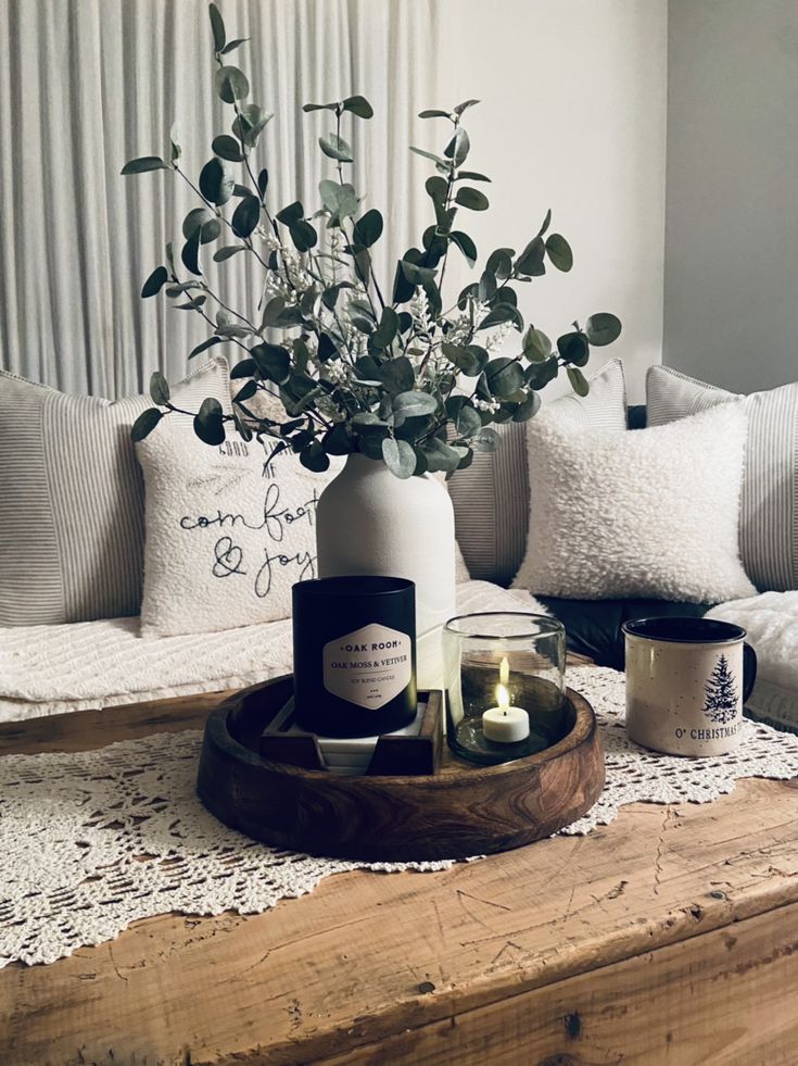 a wooden tray with candles and flowers in it on a table next to a couch