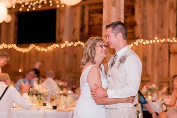 a bride and groom dance at their wedding reception in a barn with lights on the ceiling