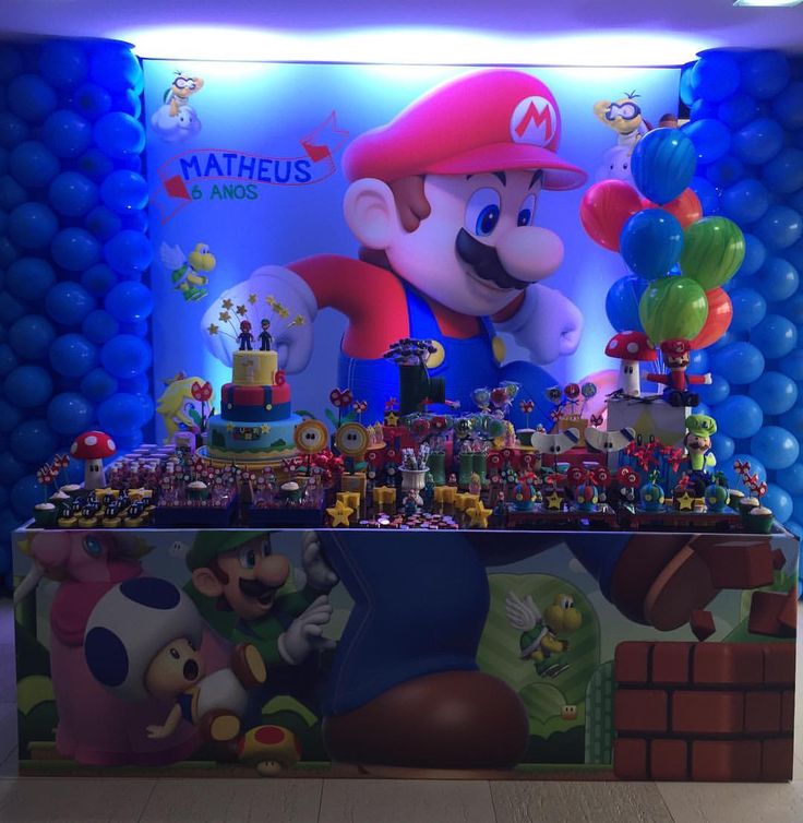 a mario birthday party setup with balloons and decorations on the wall, including an over - sized cake