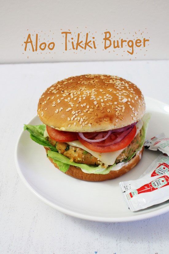 a chicken burger with lettuce, tomato and onion on a white plate next to a packet of ketchup