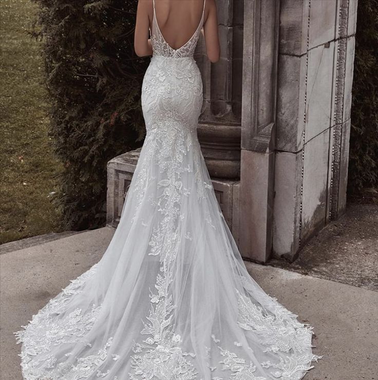 a woman in a white wedding dress is standing near an archway and looking at her back