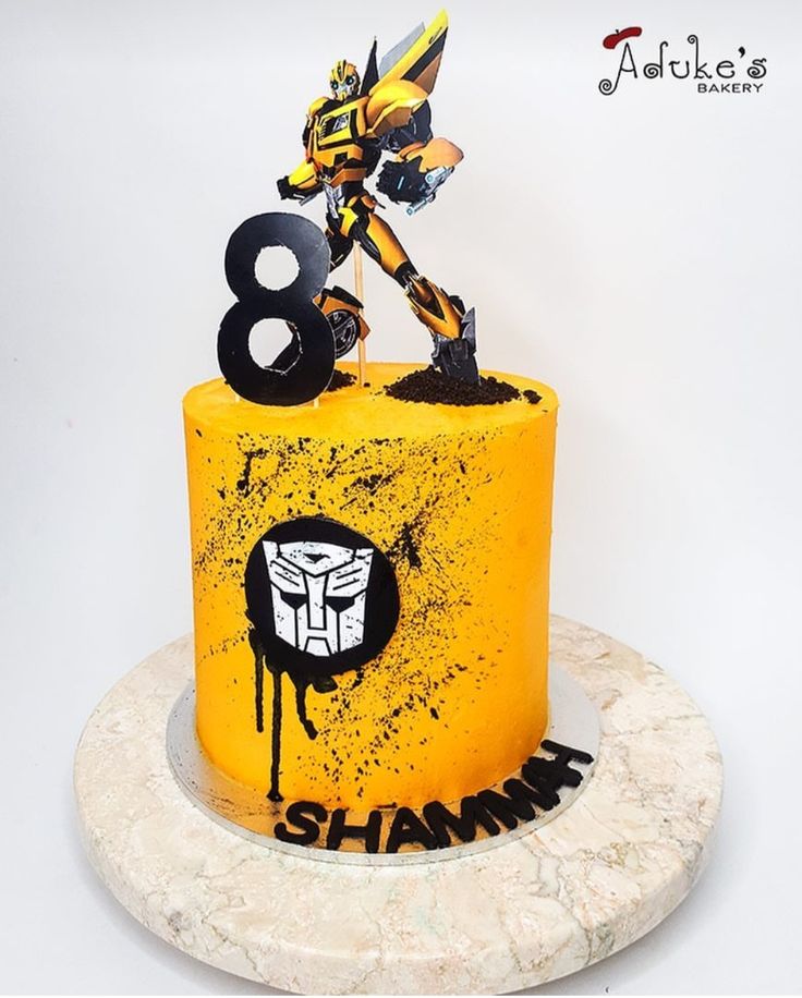 a yellow and black birthday cake with a robot figure on it's top tier