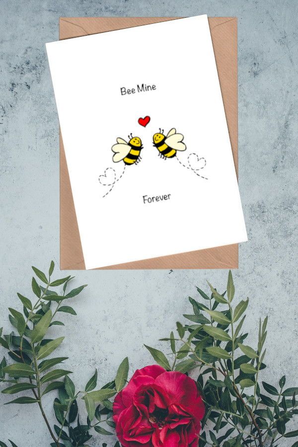 a card with two bees on it next to some flowers and a red rose in the foreground