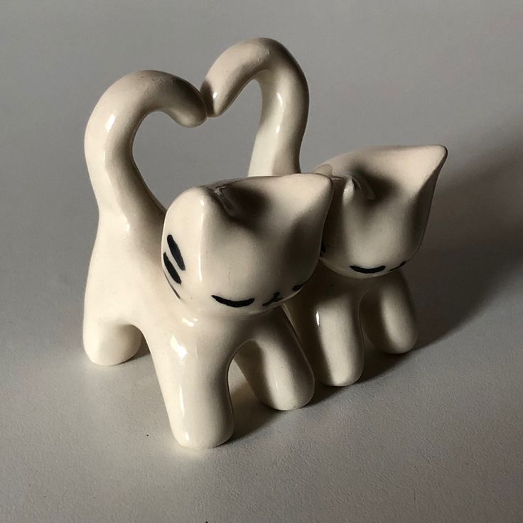 two white ceramic elephants with their trunks in the shape of a heart