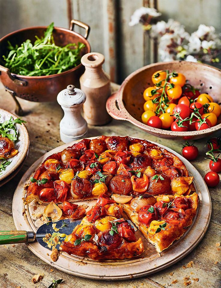 a pizza sitting on top of a wooden table next to bowls of vegetables and fruit