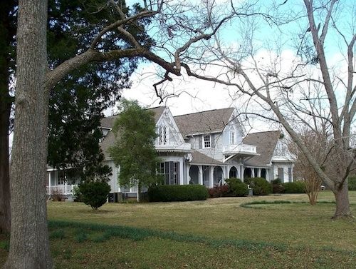 a large white house sitting in the middle of a lush green field next to trees