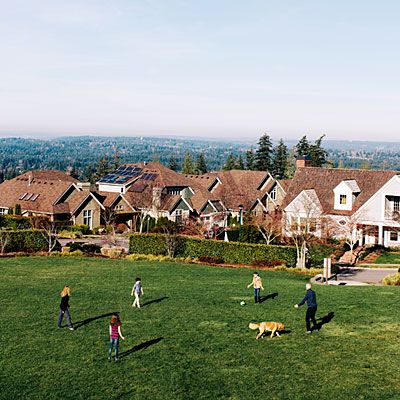 a group of people playing frisbee in a field with houses and trees behind them