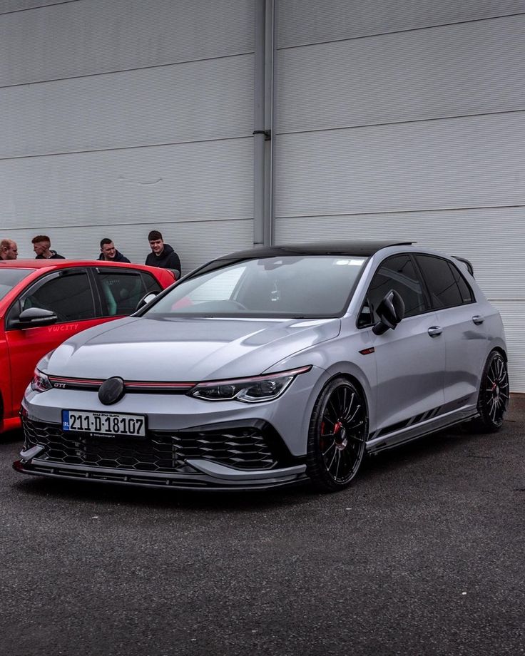 two cars parked next to each other in front of a building with people looking at them