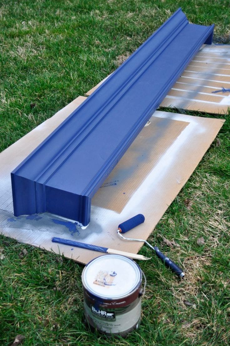 the paint is being applied to the base of an outdoor bench in the grass, next to a can of paint and a brush