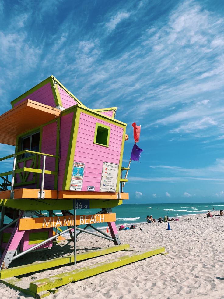 a lifeguard stand on the beach with people in the water and blue skies above