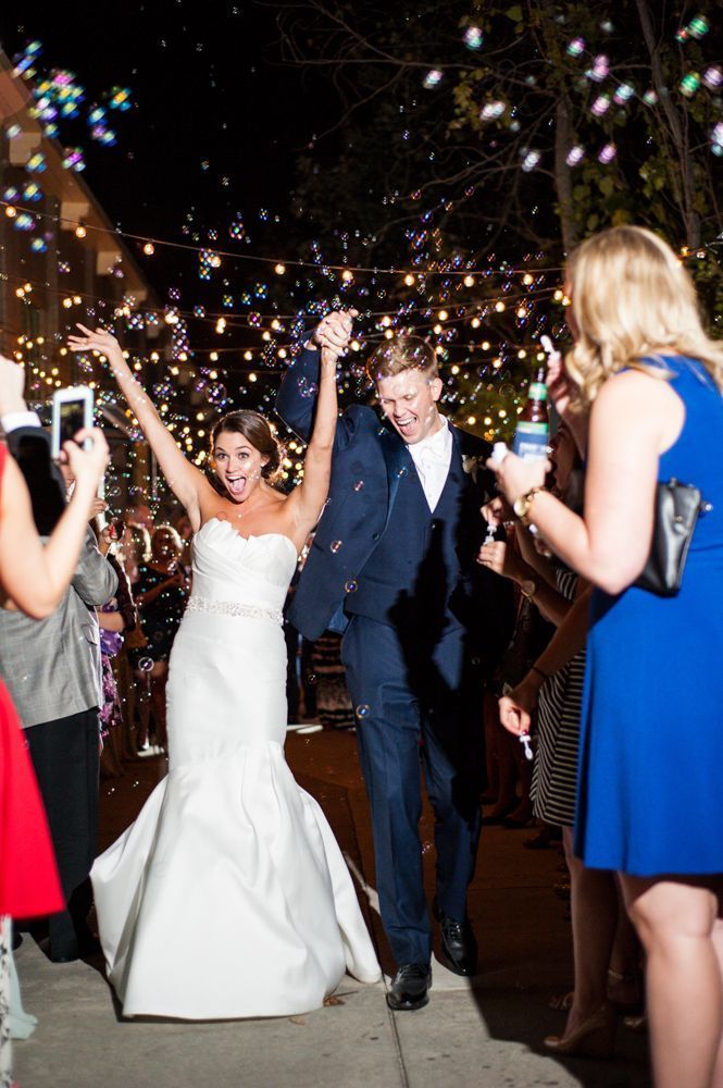 a bride and groom walk through confetti as they exit their wedding ceremony at night