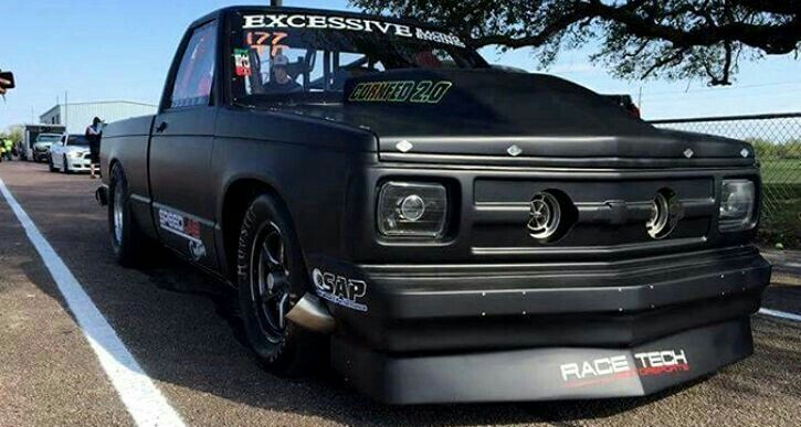 a black truck parked on top of a parking lot next to a tall fenced in area