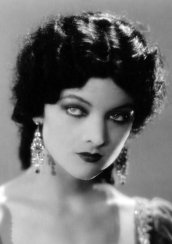 an old black and white photo of a woman with dark hair wearing large dangling earrings