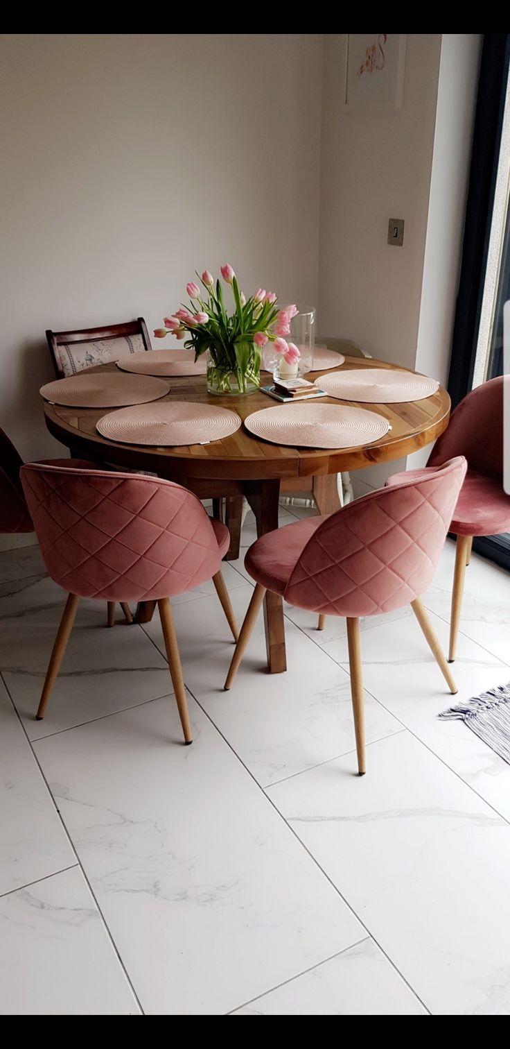 a round table with pink chairs around it and a vase filled with flowers on top