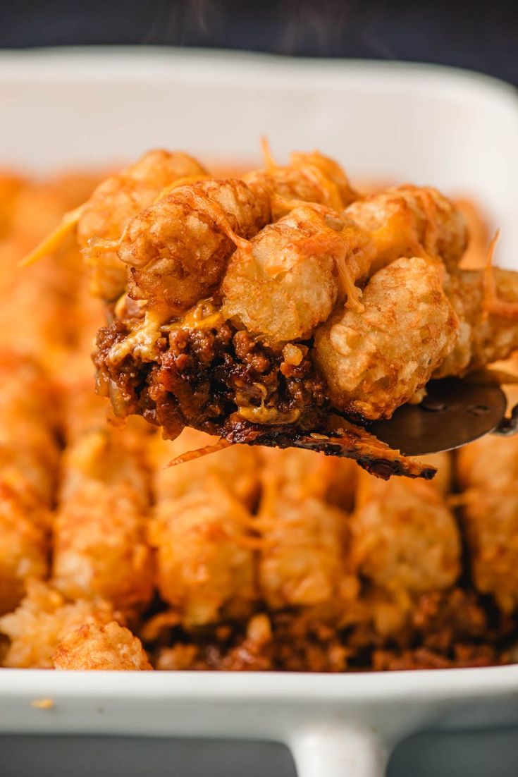 a spoon full of tater tots being lifted from a casserole dish