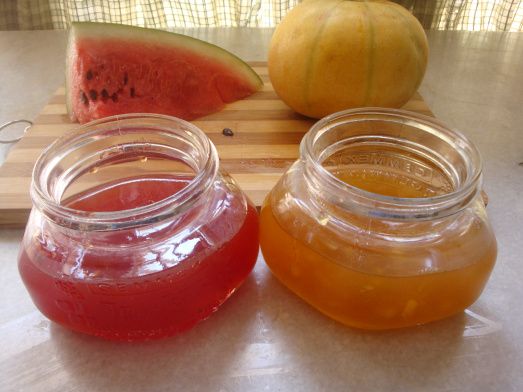 three jars filled with liquid sitting on top of a cutting board next to watermelon