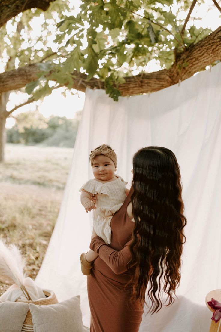 a woman holding a baby under a tree