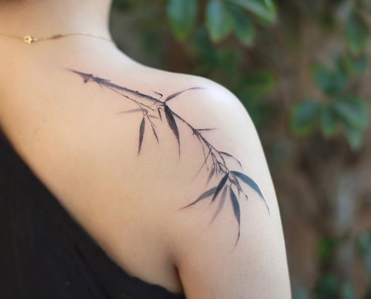 the back of a woman's shoulder with a branch tattoo on it