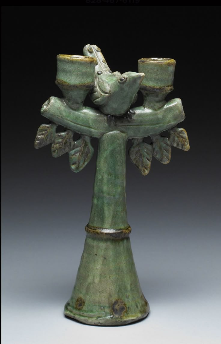 a green vase with two birds perched on it's sides and three cups in the middle