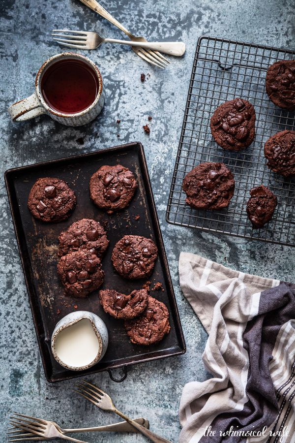 chocolate cookies cooling on a baking sheet next to a cup of tea and silverware