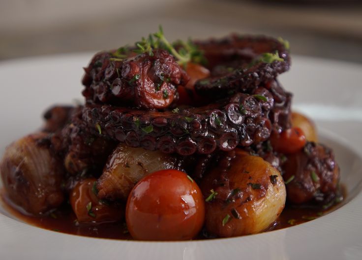 a close up of a plate of food with meat and vegetables on it, covered in sauce