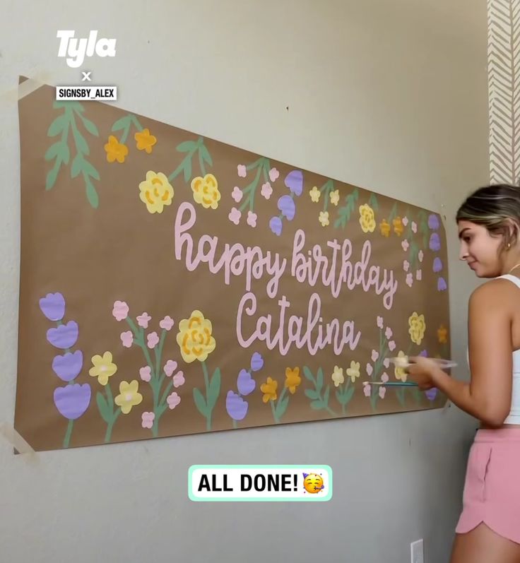 a woman is painting a sign with flowers on it that says happy birthday, claudia