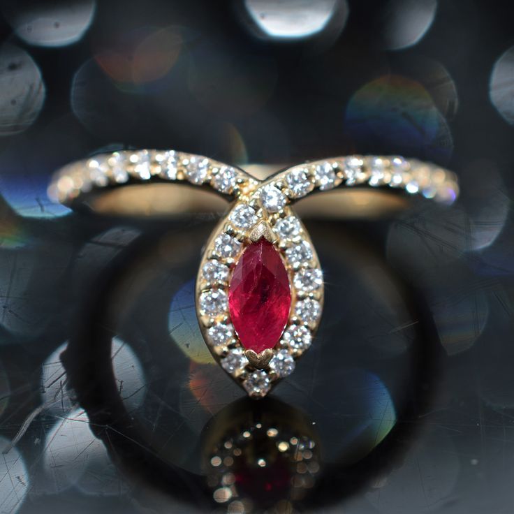 a close up of a ring with a red stone in the middle and diamonds around it