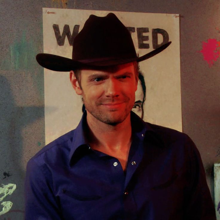 a man wearing a cowboy hat standing in front of a sign