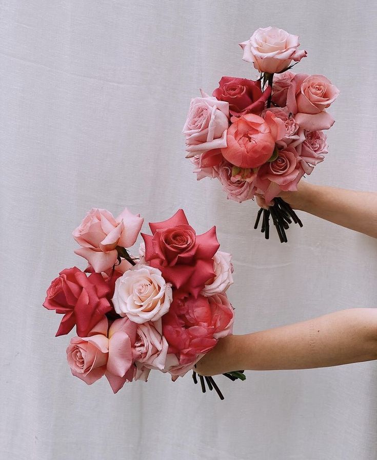 two hands holding bouquets of pink and red flowers