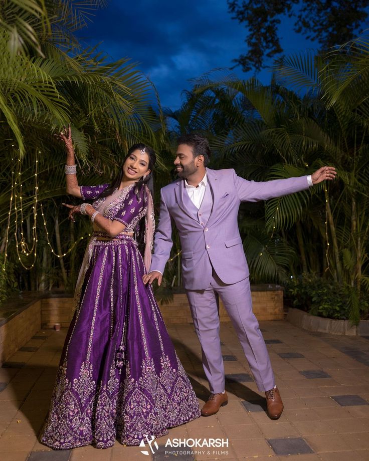 a man and woman dressed in purple posing for the camera at their wedding reception with palm trees behind them