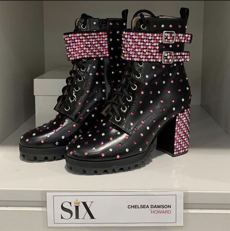 a pair of black boots with pink and white polka dots on them sitting on top of a shelf