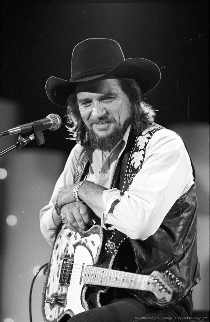 a black and white photo of a man wearing a cowboy hat while playing an acoustic guitar