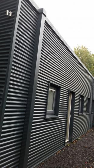 the side of a building that has black siding on it and is next to some trees