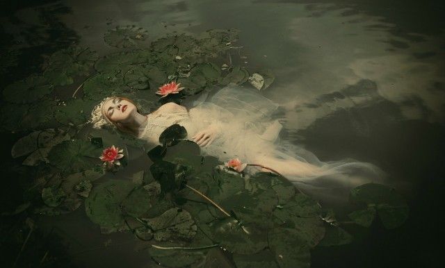 a woman laying on top of a body of water surrounded by lily pads and leaves