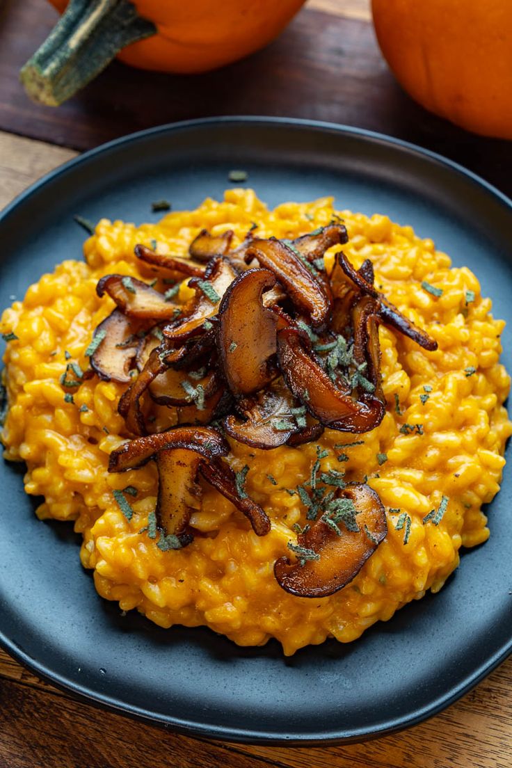 a blue plate topped with riso covered in cheese and mushrooms next to two pumpkins