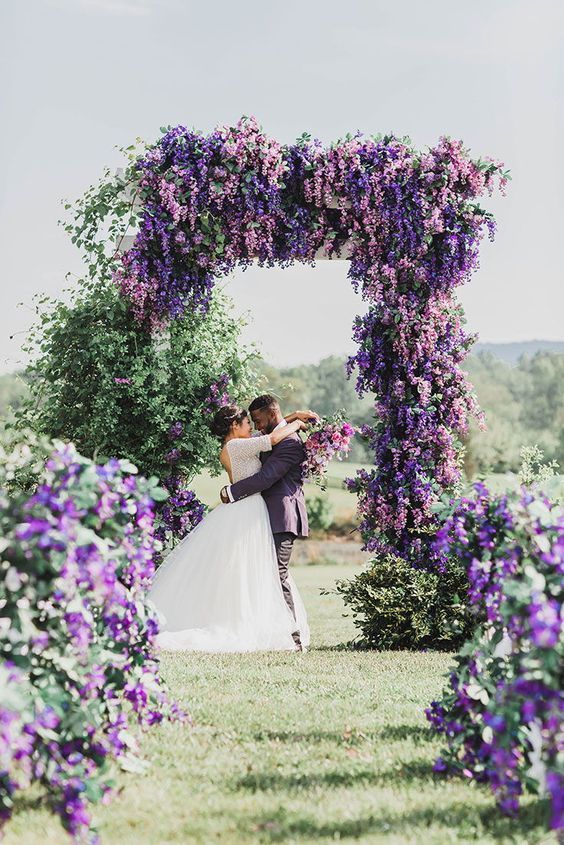 a bride and groom standing under an archway covered in purple flowers at the end of their wedding day