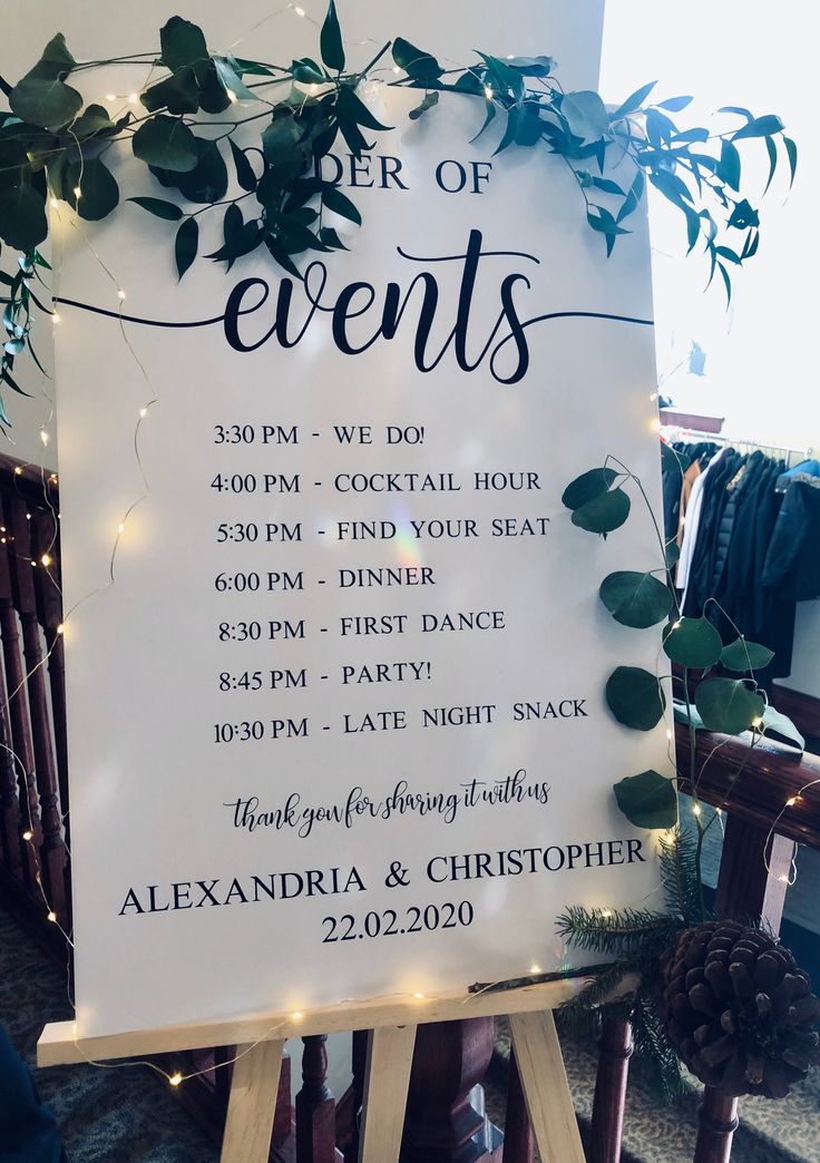 a white sign with greenery on it sitting in front of a wooden easel