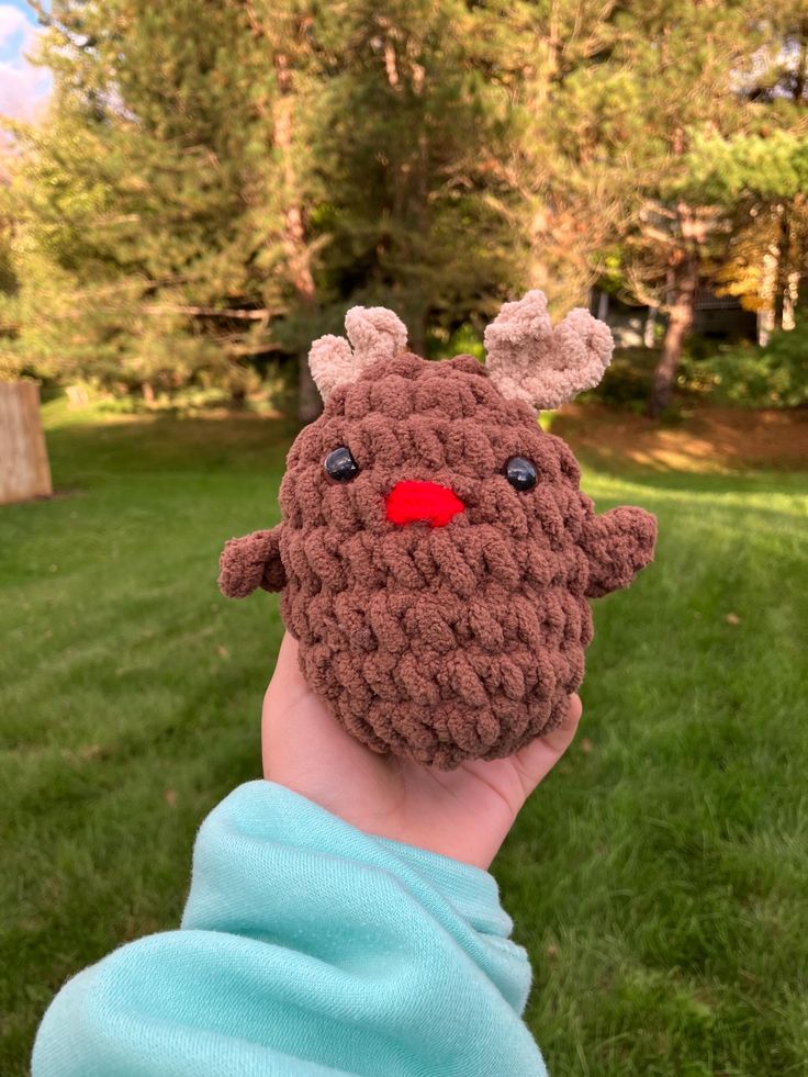 a child's hand wearing a brown crocheted reindeer hat with red nose