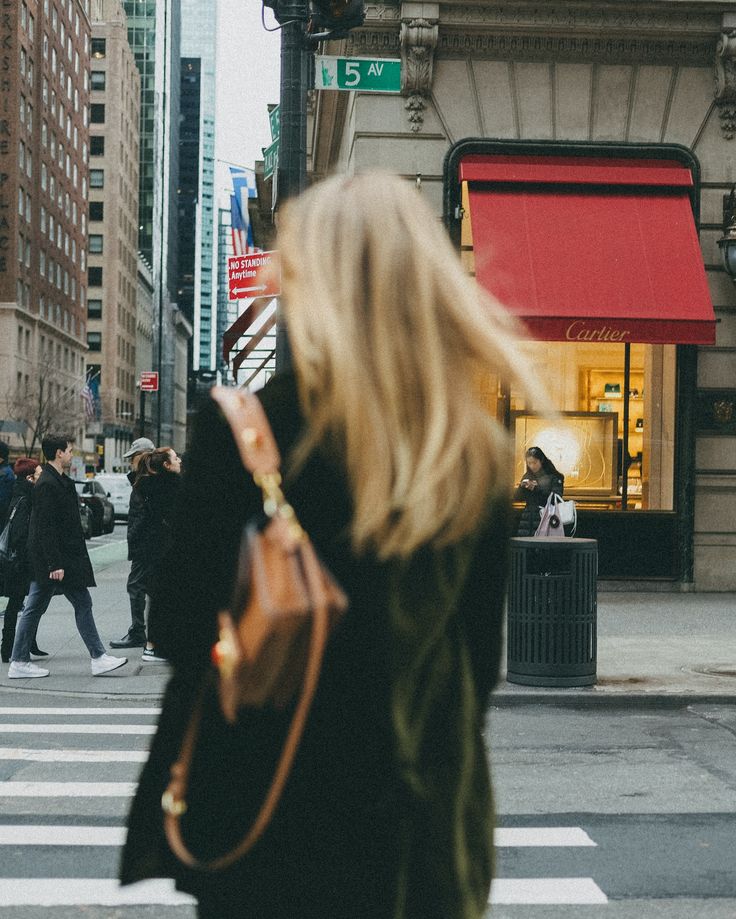 a woman walking across a cross walk in front of a store on a busy city street