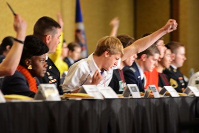 a group of people sitting at a table with their arms in the air and one person raising his hand