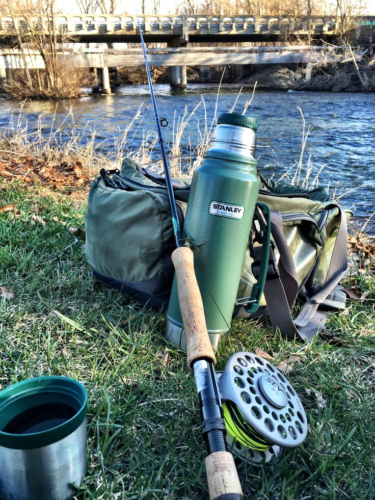 there is a fishing rod, reel and water bottle on the grass by the river