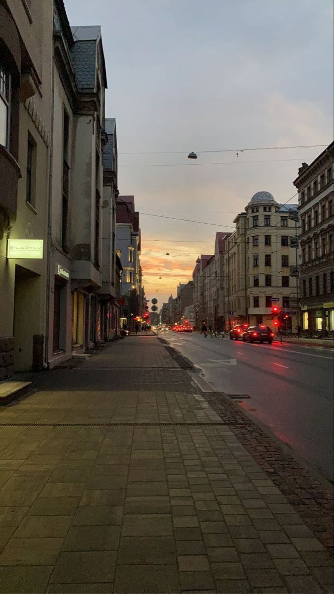 an empty city street at dusk with cars parked on the side and buildings in the background