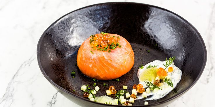 an egg and salmon dish in a black bowl on a marble counter top with garnishes