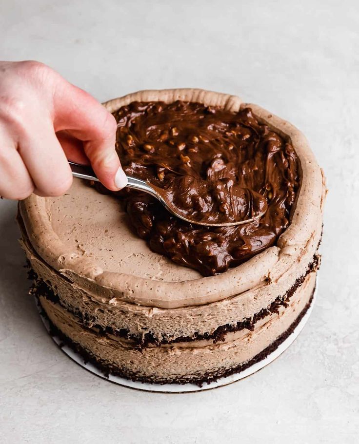 a person is spooning chocolate frosted cake from a round cake on a plate