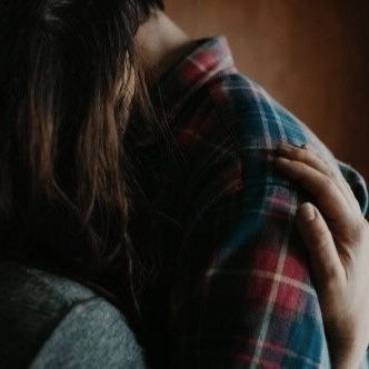 a woman is hugging her back while wearing a plaid jacket and holding onto the pillow