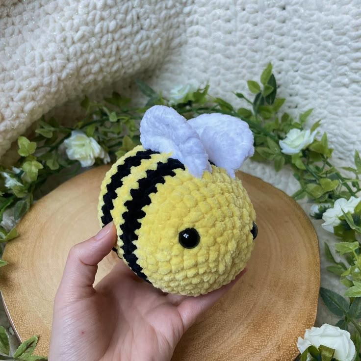 a hand is holding a small yellow and black stuffed animal with a bee on it's head