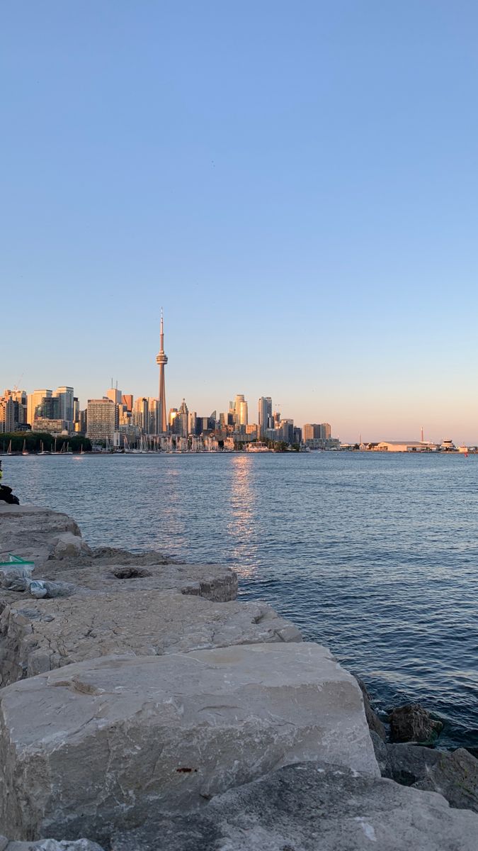 a man sitting on the edge of a rock wall next to water with a city in the background